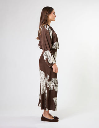Woman in a brown long-sleeved maxi dress with white floral print, side view