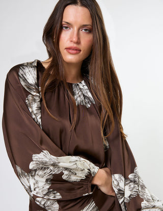 Woman wearing a brown satin long-sleeve dress with white floral prints.