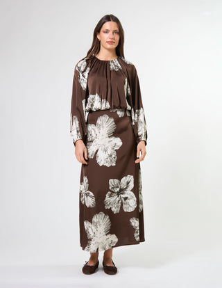 Woman wearing a long-sleeved brown maxi dress with white floral prints and brown flats.