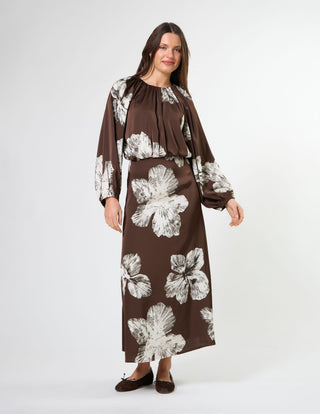 Woman wearing a brown long-sleeve midi dress with white floral prints and brown flats.