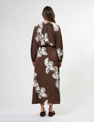 Woman wearing a brown long-sleeve maxi dress with large white floral patterns.