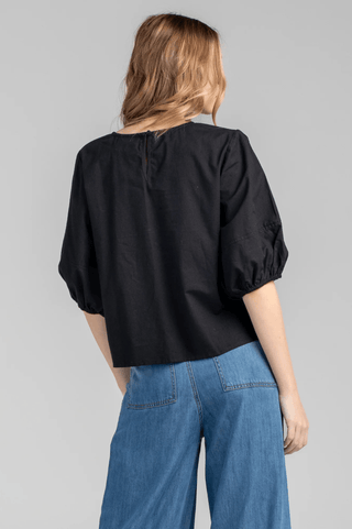 Back view of a woman wearing a black puff sleeve top and blue wide leg jeans.