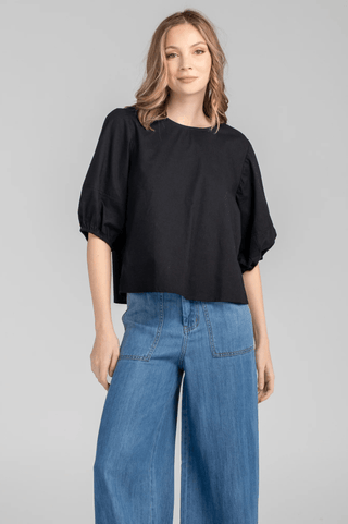 Woman wearing a black short-sleeved blouse and wide-leg blue denim jeans.