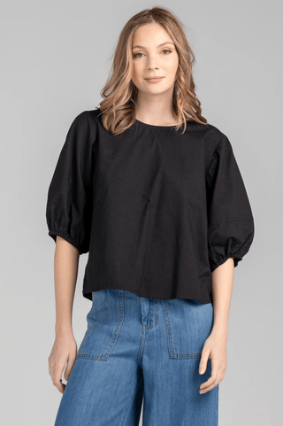 Woman wearing a black puff sleeve top and blue wide leg jeans.
