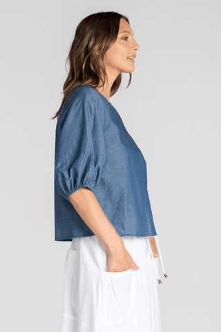 Woman wearing a blue short-sleeve linen blouse and white linen trousers.