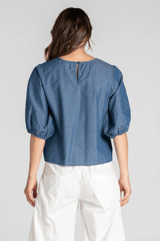 Back view of a woman wearing a blue puff sleeve blouse and white wide-leg pants.