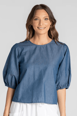 Woman wearing a blue denim puff sleeve blouse with a round neckline.