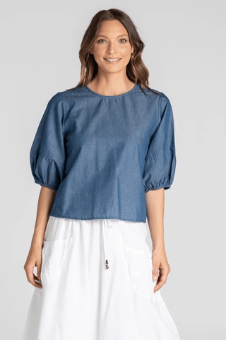 Woman wearing a blue denim puff sleeve blouse and white linen skirt.