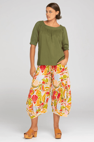 Woman wearing an olive green short sleeve top and colorful patterned palazzo pants.