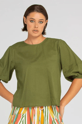 Woman wearing an olive green short sleeve linen top and colorful striped pants.