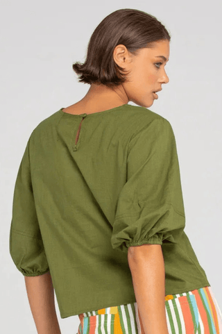 Woman wearing an olive green linen blouse with puff sleeves and a keyhole back detail.
