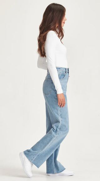 Woman wearing a white long sleeve top and light wash wide leg denim jeans with white sneakers.