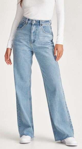 Woman wearing light blue high-waisted wide leg denim jeans and a white long sleeve top.