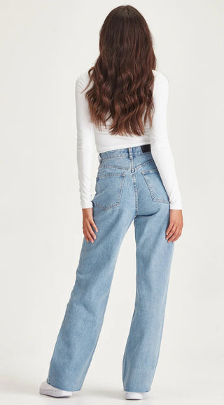 Woman wearing a white long sleeve top and light blue wide leg denim jeans.