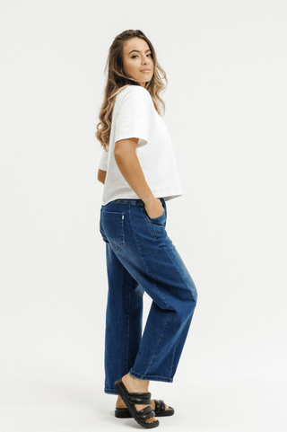 Woman wearing a white t-shirt, wide-leg blue jeans, and black sandals against a white background.