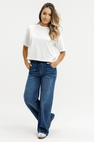 Woman wearing a white t-shirt and wide-leg blue denim jeans against a white background.