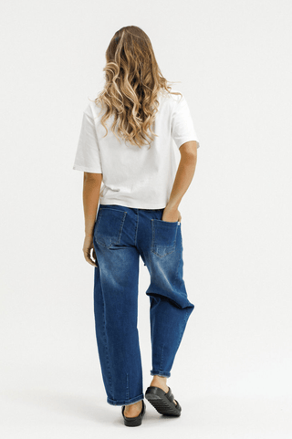 Rear view of a woman wearing a white t-shirt and wide-leg blue jeans.