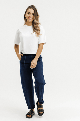 Woman wearing a white t-shirt and navy blue drawstring apartment pants with black sandals.