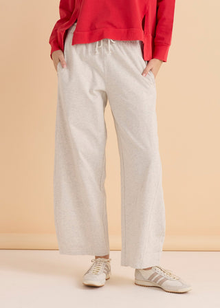 Woman wearing light grey wide leg apartment pants and a red sweatshirt with white sneakers.