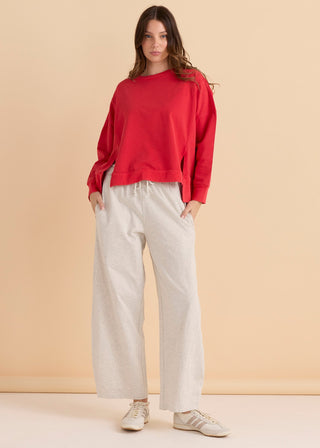 Woman wearing a red long sleeve sweatshirt and cream wide leg lounge pants.