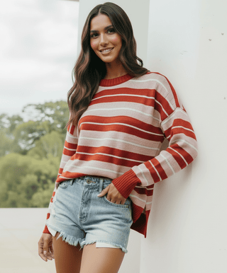 Woman smiling in a red and beige striped sweatshirt and denim shorts
