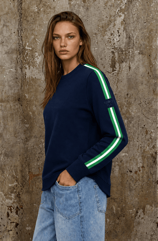 Woman wearing a navy blue sweatshirt with green and white side stripes and light blue jeans.