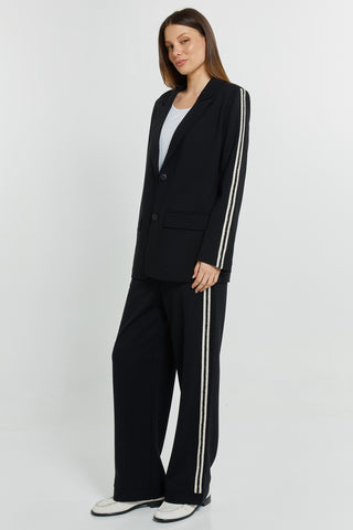 Woman wearing a black oversized blazer and wide-leg trousers set with white side stripes.