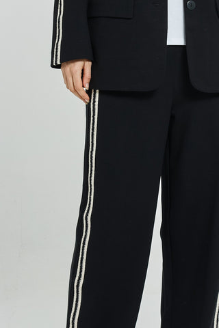 Close-up of a woman wearing a black blazer and matching pants with white side stripes.