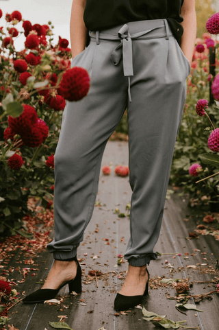 Woman wearing grey high-waisted jogger pants with a tie waist and black pointed heels.
