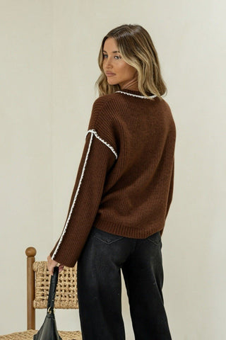 Woman wearing a brown ribbed knit sweater with white trim and black wide-leg pants.