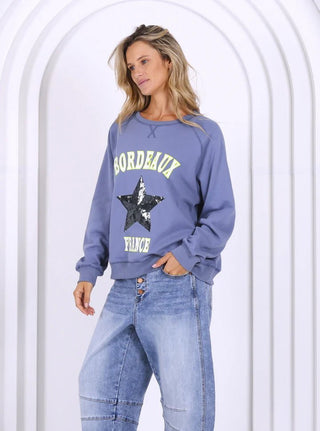 Woman wearing a blue Bordeaux France sweatshirt with a sequin star and light wash jeans.