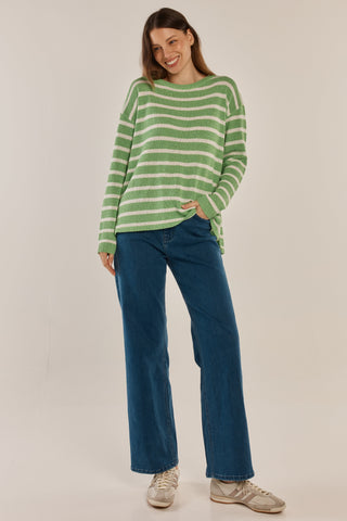 Woman wearing a green and white striped sweater with wide-leg blue jeans and white sneakers.