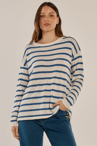 Woman wearing a white and blue striped knit sweater and blue jeans.