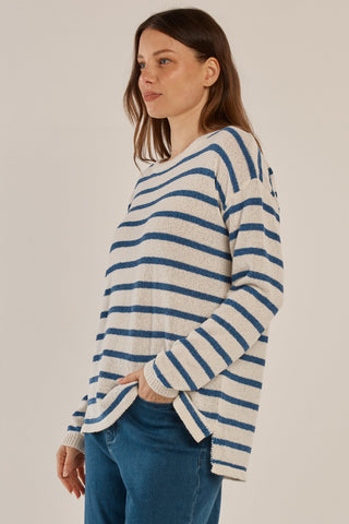 Woman wearing a white and blue striped knit sweater and blue jeans.