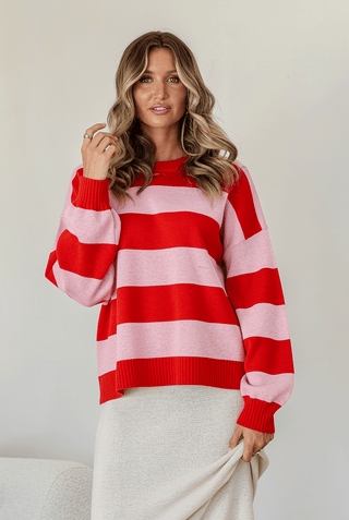 Woman wearing a red and pink striped knit sweatshirt and cream skirt.