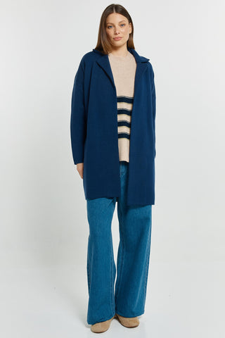Woman wearing a navy blue coat over a beige striped sweater and blue wide-leg denim jeans.