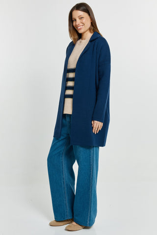 Woman wearing a navy blue coat over a beige striped sweater and blue wide-leg jeans.