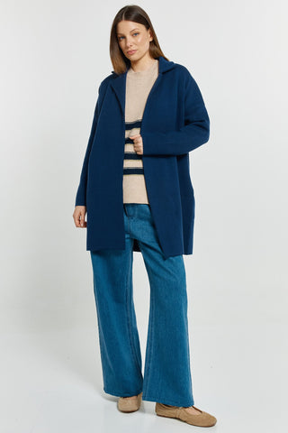 Woman wearing a navy blue coatigan, striped beige sweater, and blue flared denim jeans.