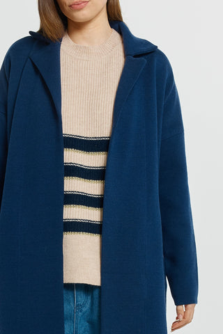 Woman wearing a navy blue longline coat over a beige striped knit sweater and blue jeans.