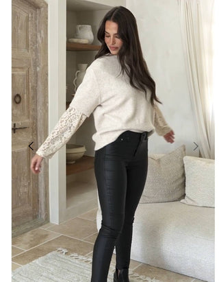 Woman wearing a cream knit sweater with lace sleeves and black faux leather pants.