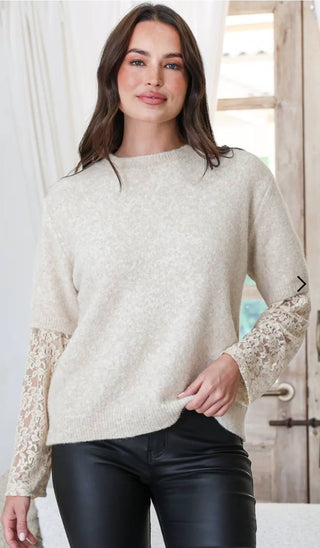 Woman wearing a cream knit sweater with long lace sleeves and black leather pants.