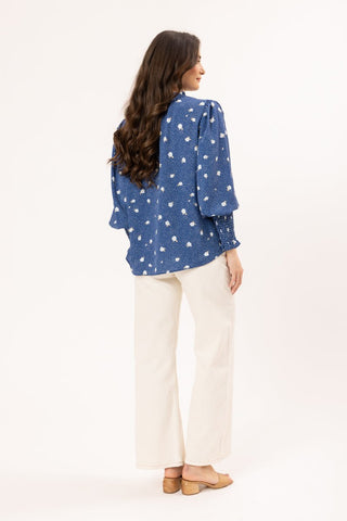 Woman wearing a blue floral print long sleeve blouse and white wide leg pants.
