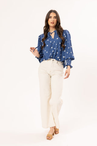 Woman wearing a blue floral tie-neck blouse and cream wide-leg pants.