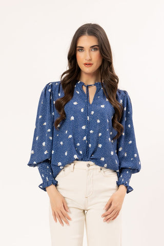 Woman wearing a blue floral polka dot blouse with puff sleeves and cream trousers.