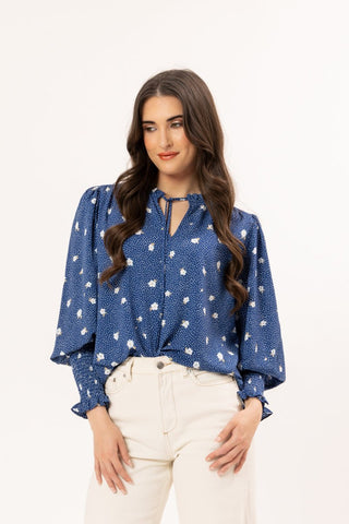 Woman wearing a blue long sleeve floral print blouse and white pants.