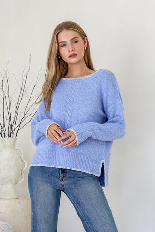 Woman wearing a light blue cable knit sweater and blue jeans.