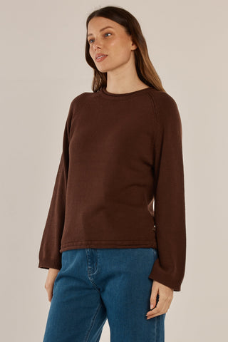 Woman wearing a brown long sleeve crewneck sweatshirt and blue denim pants.