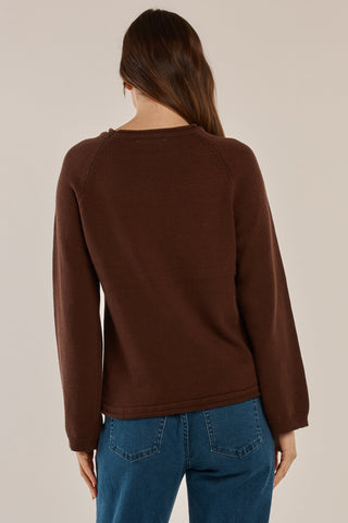 Back view of a woman wearing a brown long-sleeve knit sweatshirt and blue denim jeans.