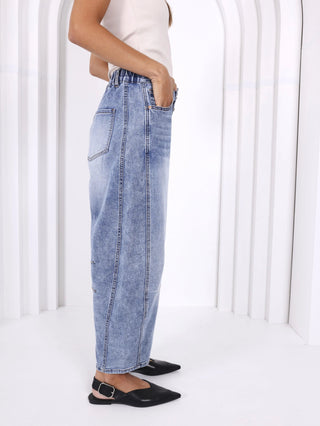 Woman wearing light wash wide leg denim jeans and black pointed toe flats.