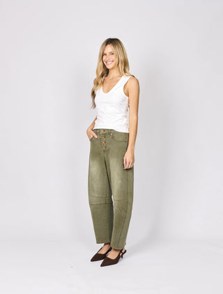 Woman wearing a white tank top and olive green button-fly pants with brown pointed heels.